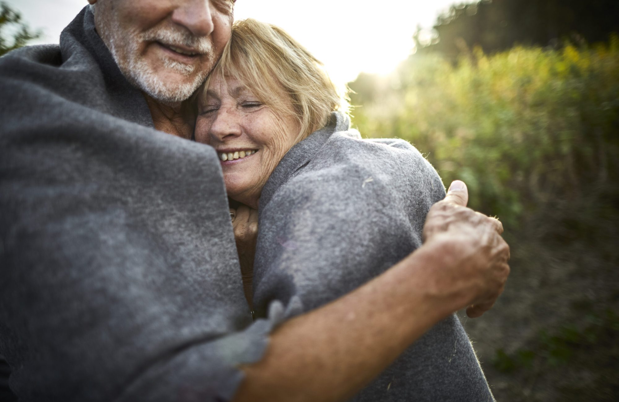 Mature couple wrapped in a blanket cuddling in the countryside